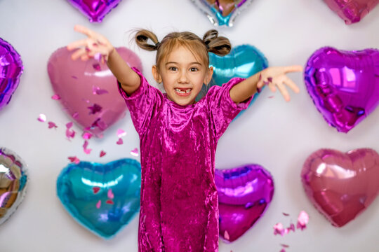 Funny laughing girl throws pink confetti in the shape of hearts. Happy Valentine's Day Greetings