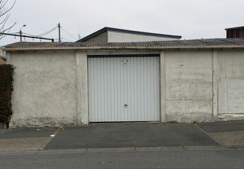 Fototapeta premium Closed white metal garage door on old concrete building facade with asphalt driveway