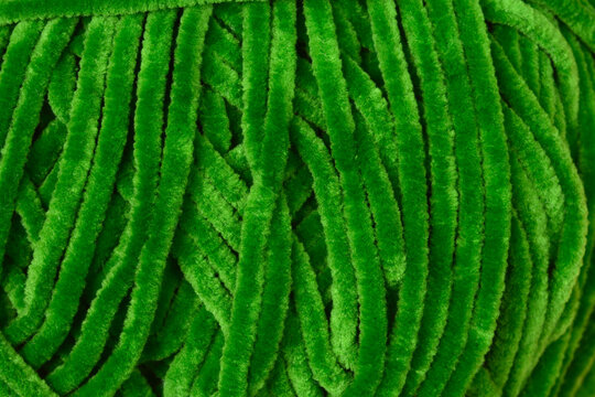 A high angle macro shot capturing the soft plush texture and vivid green color of a velvet chenille yarn ball used for knitting and handmade crafts