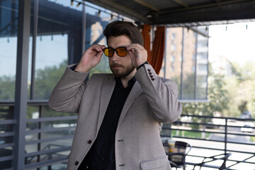 Man in a jacket adjusting his sunglasses outdoors.