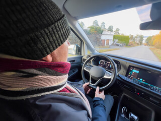 Calm strength senior lifestyle with an older man driving a modern car from rear seat view in daylight, hands on steering wheel, winter clothing, quiet everyday mobility and independent life after 60.