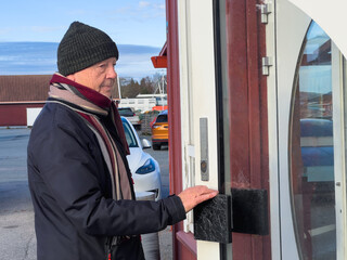 Everyday independence senior lifestyle with an older man opening a local shop door in the daytime, winter clothing and calm posture, slow living routine and active life after 60.