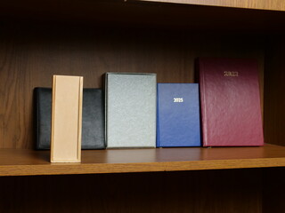 Row of notebooks and planners from different years on wooden shelf, personal records storage