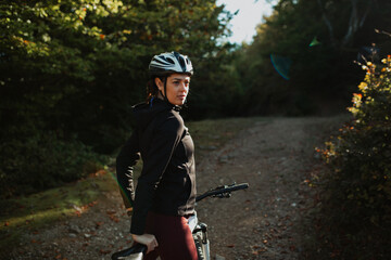 Portrait of a sporty girl with her bike in the forest, wearing a safety helmet