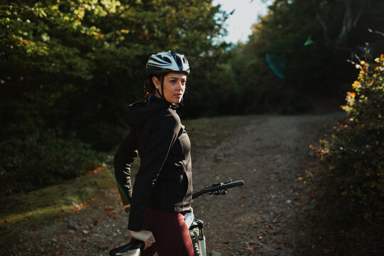 Portrait of a sporty girl with her bike in the forest, wearing a safety helmet