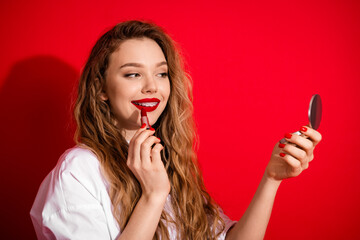 Chic Woman Applying Red Lipstick with Mirror on Red Background Showcasing Beauty and Glamour
