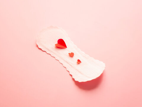 Sanitary pad with red paper hearts on pink background concept of menstruation and feminine hygiene