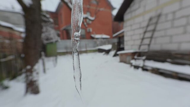 Drops of water drip from an icicle hanging on a gutter.