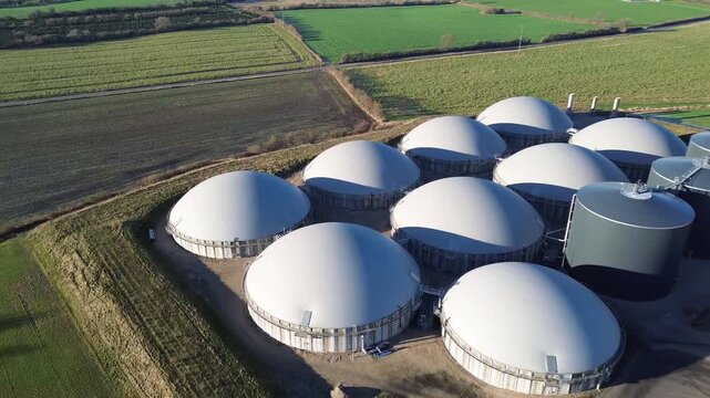 Biogas facility in rural Denmark featuring dome-shaped digesters and storage tanks. The plant is integrated into the agricultural landscape and represents sustainable energy production through anaerob