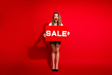 Woman Holding Sale Sign Against Vibrant Red Background Promoting Exciting Discounts and Holiday...
