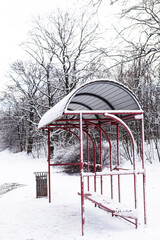 Bus stop with a roof near a forest surrounded by snow on a winter day