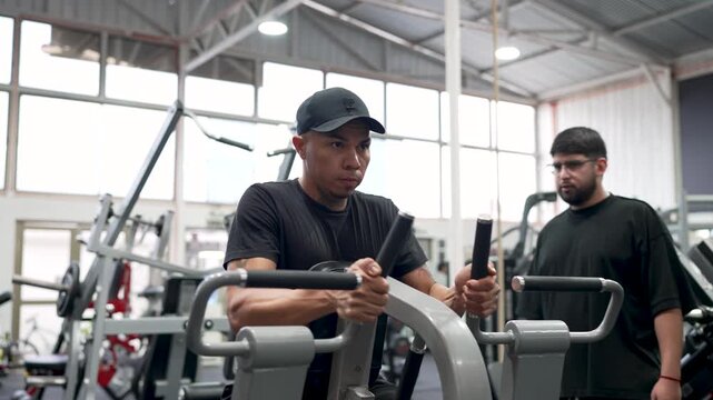 Young man using a seated rowing machine while his personal trainer supervises his back workout