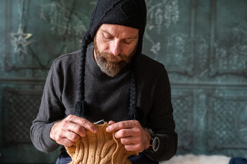 Bearded man knitting wool garment at home, cozy slow living lifestyle