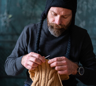 Bearded man knitting wool garment at home, cozy slow living lifestyle