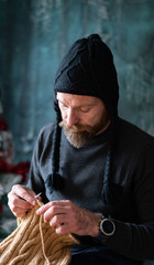 Bearded man knitting wool garment at home, cozy slow living lifestyle
