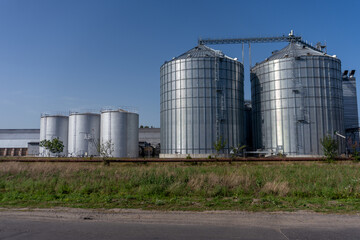 Two large metal silos are located next to a road in an industrial area. The clear blue sky provides a backdrop to the structures © Роман Булатов