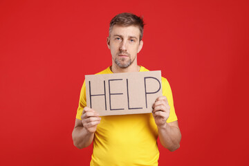 Unhappy man holding cardboard sign with word Help on red background