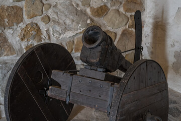 An old displayed medieval cannon with wheels in the stone interior of a castle.

