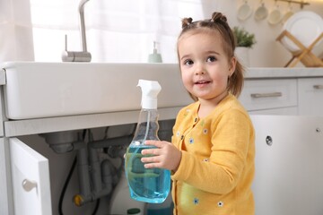 Child safety at home. Little girl with bottle of cleaning product in kitchen
