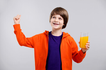 Boy with glass of fresh orange juice showing strength on light grey background