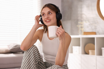 Naklejka premium Beautiful woman with cup of coffee listening to music at home