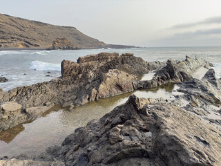 Rocky coastline with ocean waves and distant hills.. Lanzarote, Canary Islands, Spain