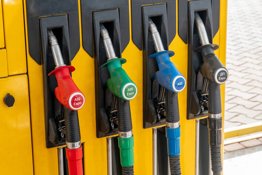 Four fuel dispensers stand at a gas station. Each dispenser has a different color nozzle. People can choose fuel types like A92, A95, and diesel