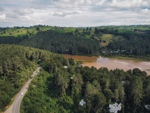 Aerial view of road crossing yarumo-dotted forest and green pastures with R&iacute;o Grande flowing through Antioquia valleys. Scenic landscape showcasing mixed-use terrain and ecological diversity 