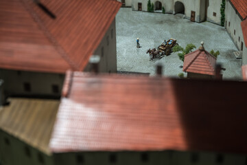 Detail of a small figurine of a carriage with horses in a courtyard with miniature figures.
