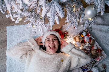 Smiling Woman in Santa Hat Enjoying Christmas Under Tree