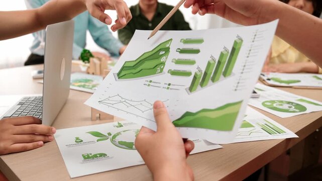 Excellent business team discuss on eco house project at messy table with green energy using graph with windmill, home, tree model for decreasing carbon usage to save earth. Focus on hand. Delineation.