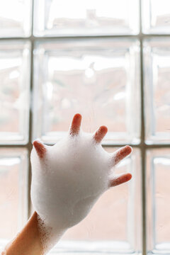 Child's Hand Covered in Bubbles in front of Window