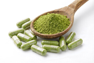 Wooden spoon holds vibrant green moringa powder beside green herbal capsules