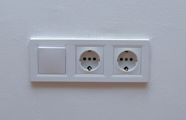 Double electrical wall socket with light switch on white wall