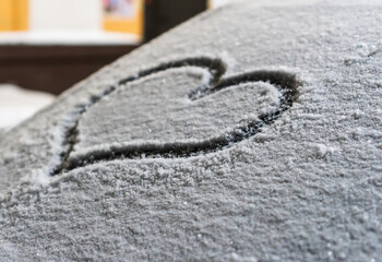 Valentine's Day concept: hand-drawn heart pattern on a frozen car windshield. Hand drawn heart shape on windshield of the car. Love symbol. Romantic background. A frozen windshield with a heart. 