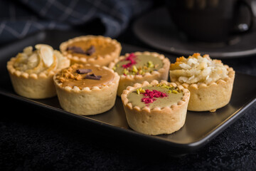 Sweet mini tartlets on plate on black table.