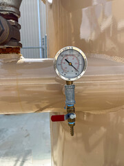 Pressure gauge attached to a storage tank in an industrial facility during daylight hours