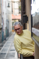 Woman in a cozy yellow sweater exploring a narrow alleyway in a quaint town during a sunny afternoon