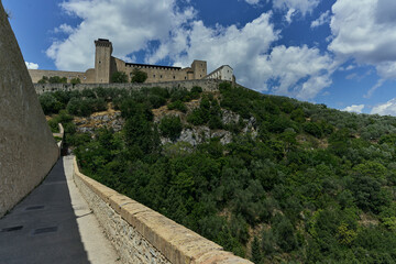 Obraz premium Medieval fortress on a steep hill, likely Rocca Albornoz in Spoleto, framed by a stone wall under a clear blue sky, Umbria, Italy.