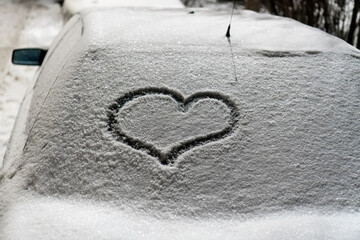 Valentine's Day concept: hand-drawn heart pattern on a frozen car windshield. Hand drawn heart shape on windshield of the car. Love symbol. Romantic background. A frozen windshield with a heart. 