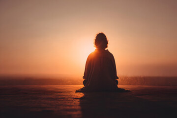 Naklejka premium Person sits in meditation while watching sunset on a quiet evening outdoors