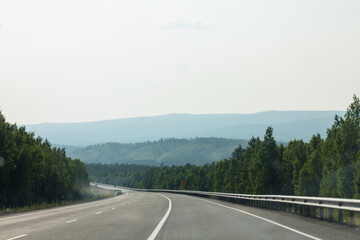 Asphalt road through the green forest. View from the car.
