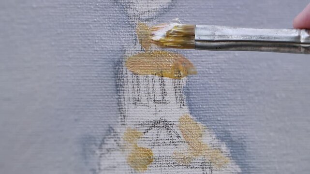 Artist painting with brush on canvas, adding yellow ochre color to artwork