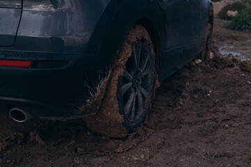 Vehicle stuck in muddy terrain, showcasing a rear wheel covered in mud, emphasizing the challenges of off-road driving and the need for proper traction in difficult conditions
