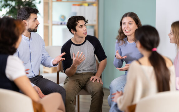 Positive young attendees of courses talking and gesturing while sitting in a circle during classes