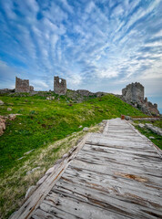 Hellenistic Attalid ruins of Temple of Trajan, Dionysus, Athena featuring wooden pathway amid green hills in Pergamon, Bergama