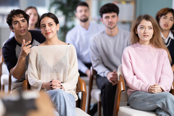 Guy listener turns to girl neighbor, talks to classmate. Young people are listening to lecture in auditorium. Personal growth courses, group psychological interaction, practical classes in psychology