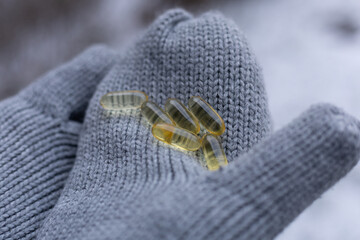 Closeup of a person wearing gloves and holding vitamin D capsules. Concept of supplementing vitamin D in winter.