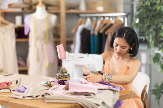 Young asian woman seamstress sewing clothes on sewing machine in workshop