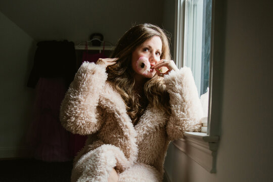 woman in fur coat biting flower 